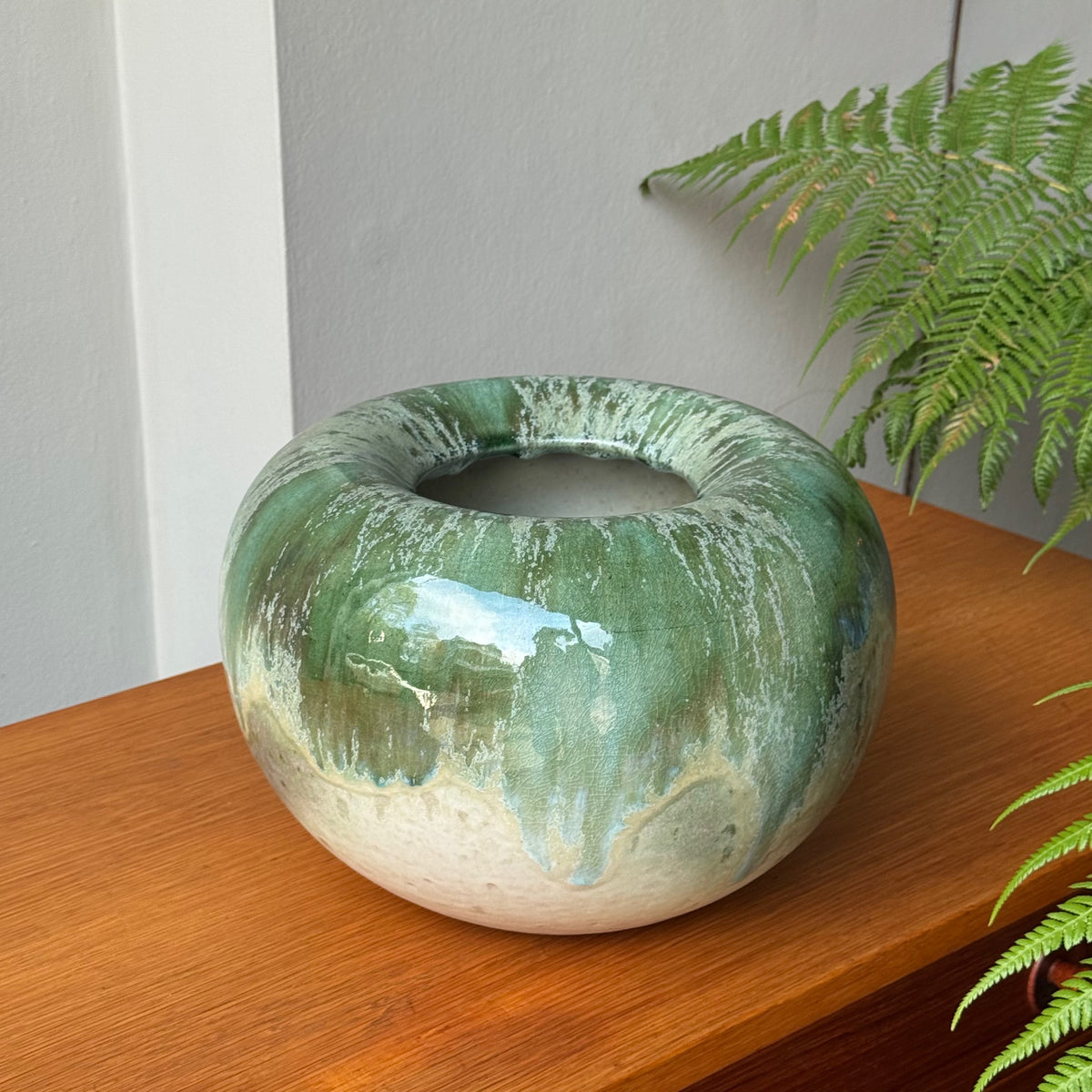 Green ceramic vase on a wooden surface with ferns in the background