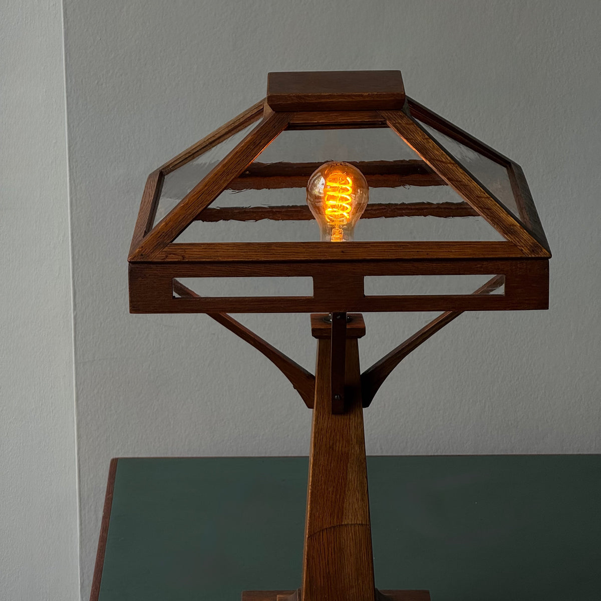 Wooden lamp with a glass shade and lit bulb against a plain background