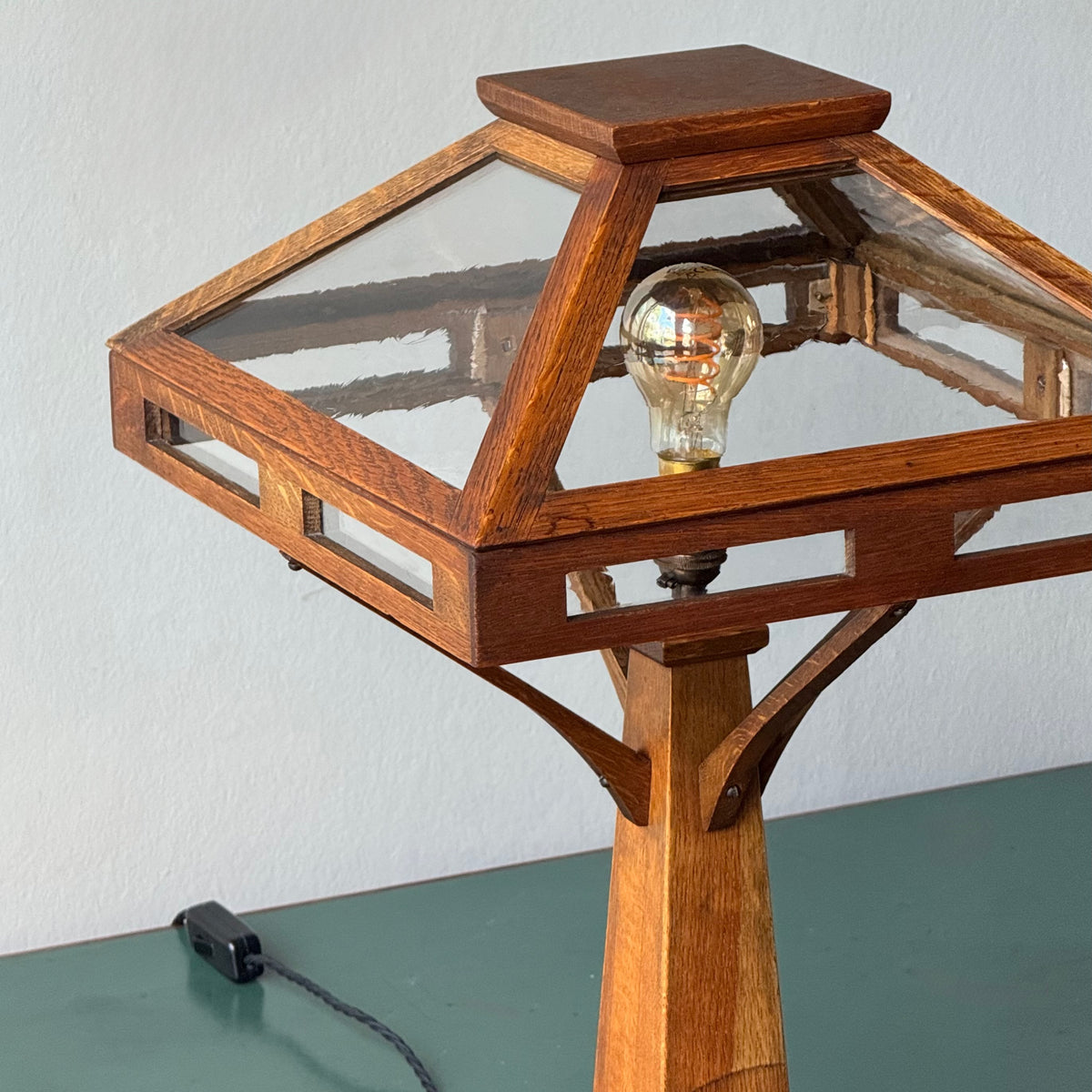 Wooden table lamp with a clear glass shade and visible bulb on a green surface.