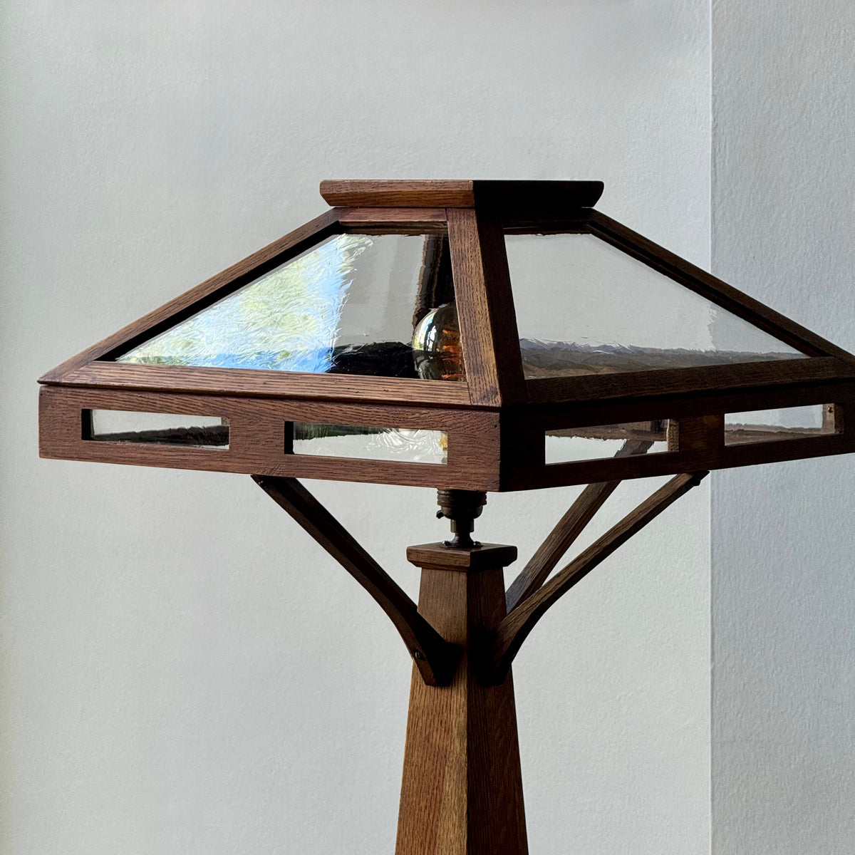 Wooden floor lamp with glass shade against a plain background