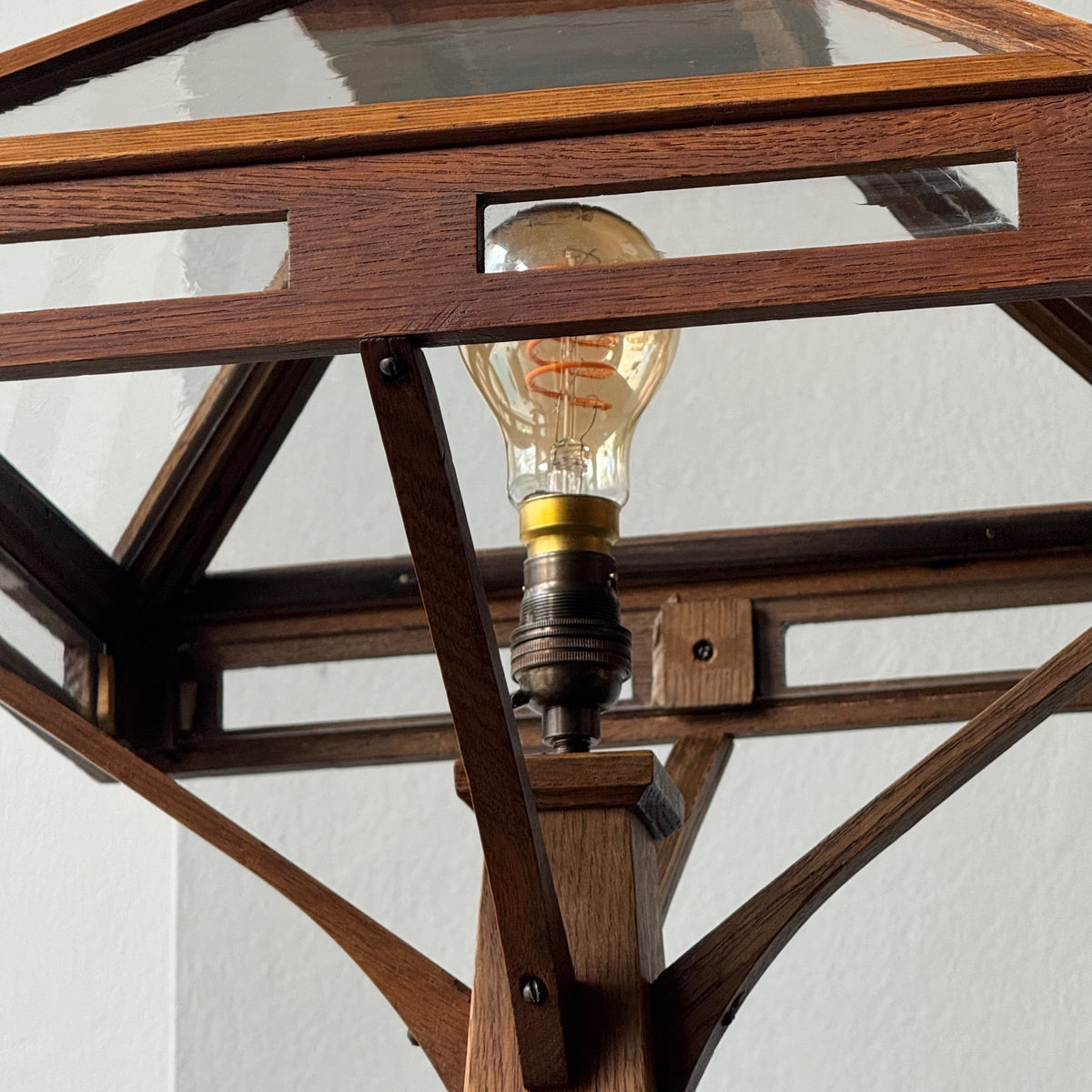 Wooden geometric lamp with a lit bulb against a white background