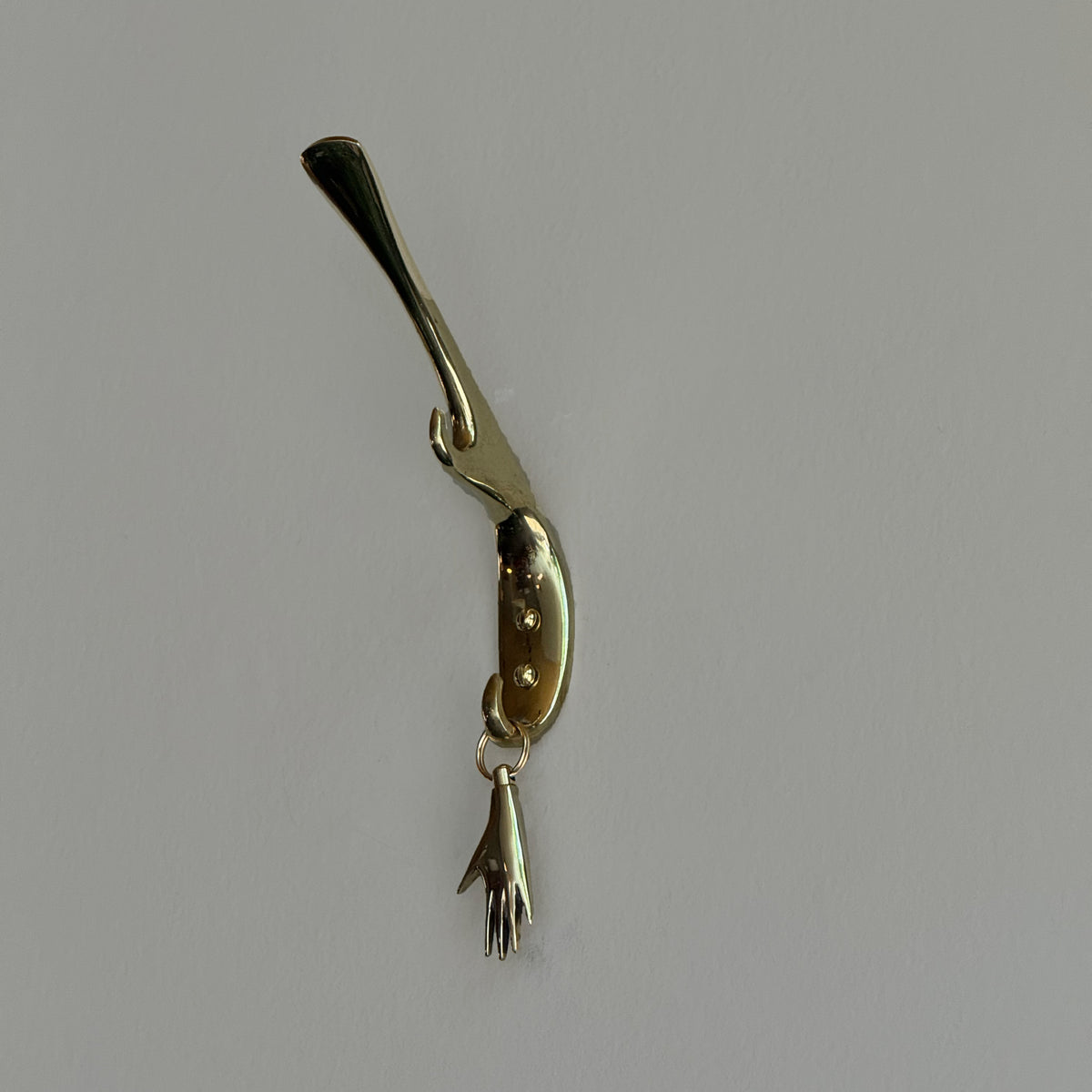 Brass Carl Aubock keyring shaped like a hand on a gray background. 