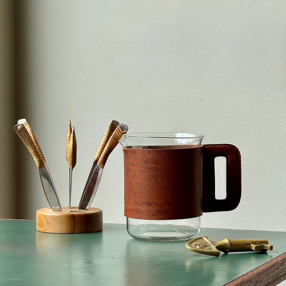 A mouth-blown glass jug with hand stitched leather sleeve handle, made and designed by Austrian designer Carl Auböck II.