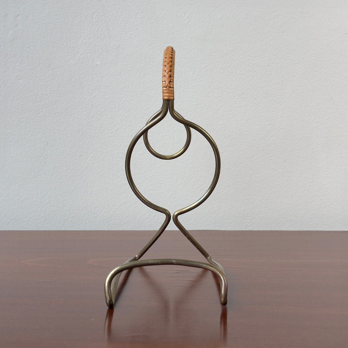 A vintage bottle holder designed by Carl Auböck II in the 1950s, made of brass with a caned accent handle. This Austrian tableware piece exemplifies minimal, functional modernist design, showcasing Auböck's attention to detail and innovative use of materials.
