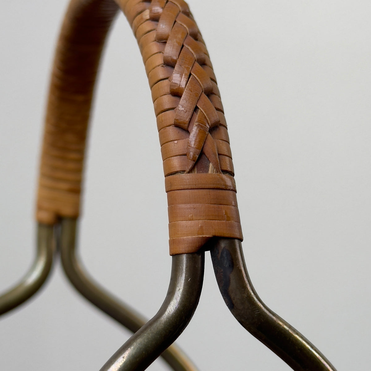 A vintage bottle holder designed by Carl Auböck II in the 1950s, made of brass with a caned accent handle. This Austrian tableware piece exemplifies minimal, functional modernist design, showcasing Auböck's attention to detail and innovative use of materials.