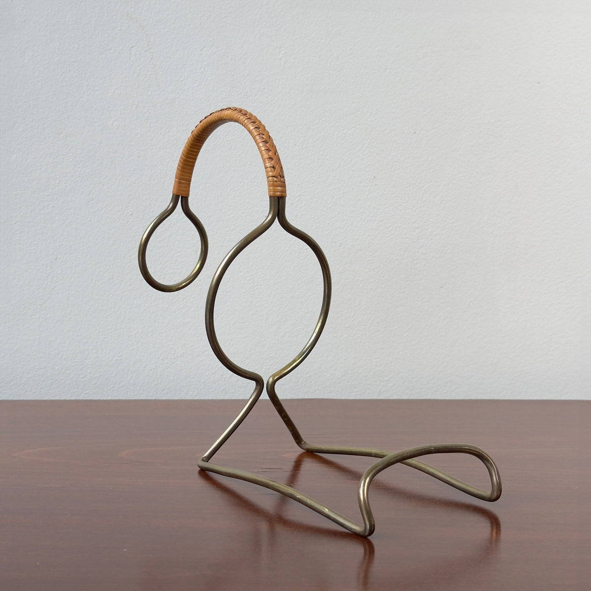 A vintage bottle holder designed by Carl Auböck II in the 1950s, made of brass with a caned accent handle. This Austrian tableware piece exemplifies minimal, functional modernist design, showcasing Auböck's attention to detail and innovative use of materials.