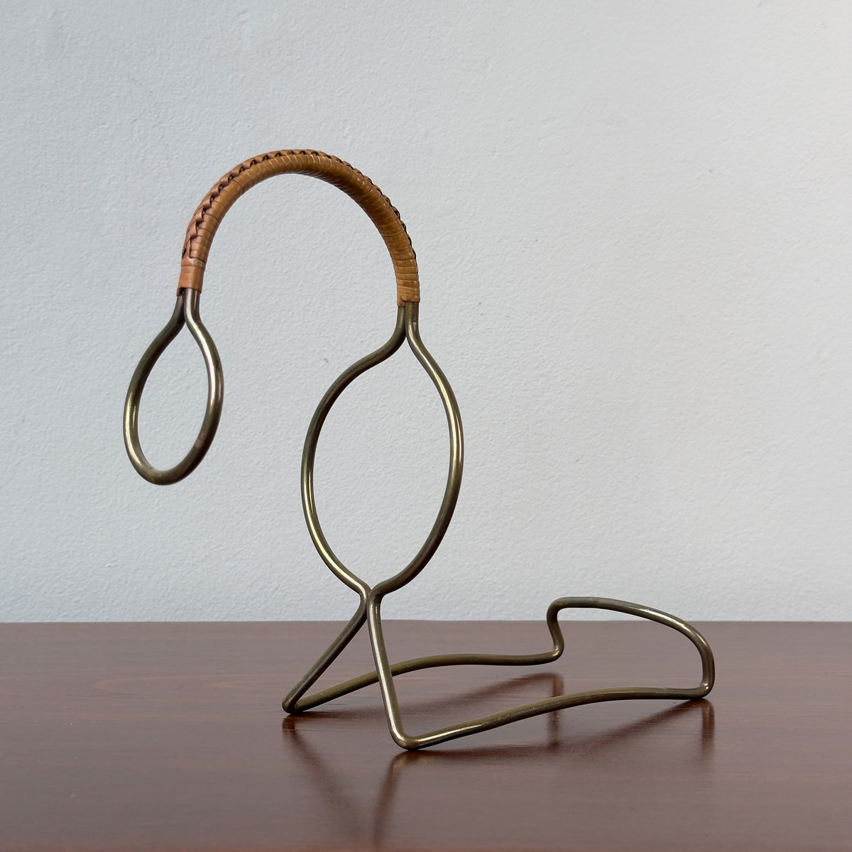 A vintage bottle holder designed by Carl Auböck II in the 1950s, made of brass with a caned accent handle. This Austrian tableware piece exemplifies minimal, functional modernist design, showcasing Auböck's attention to detail and innovative use of materials.