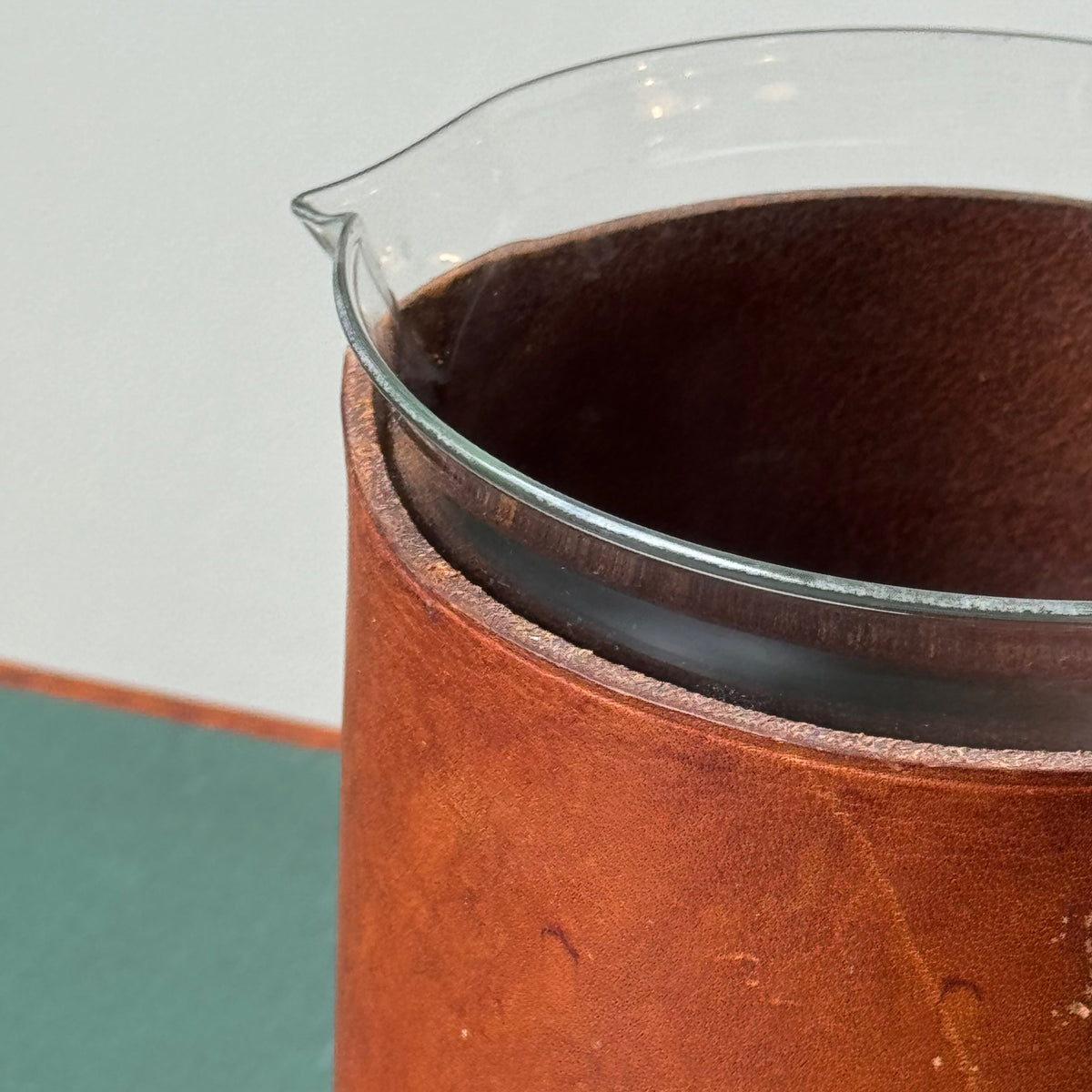 A mouth-blown glass jug with hand stitched leather sleeve handle, made and designed by Austrian designer Carl Auböck II.