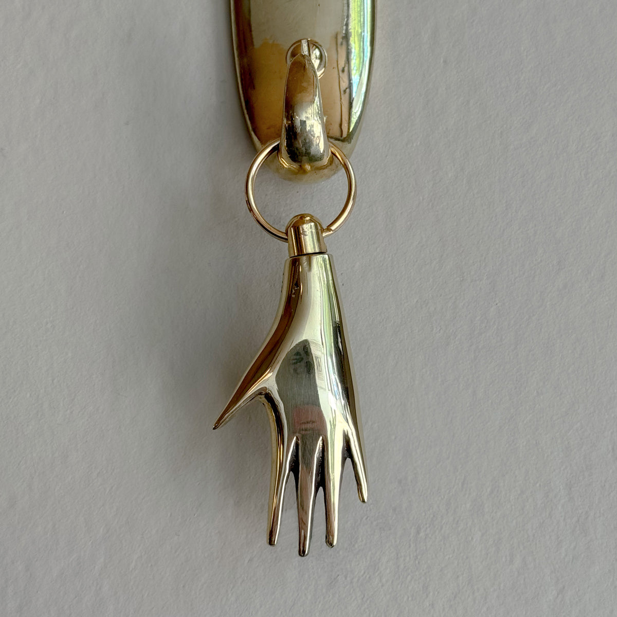 Brass Carl Aubock keyring shaped like a hand on a gray background. 