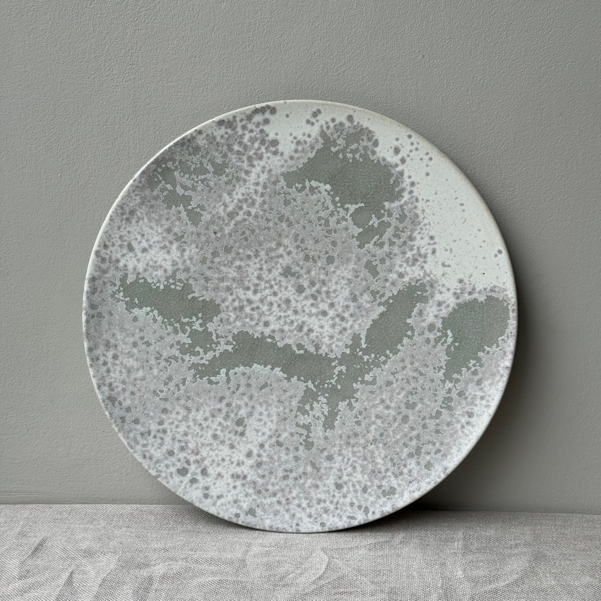 A green glazed flat plate with white undertones put up against a grey wall