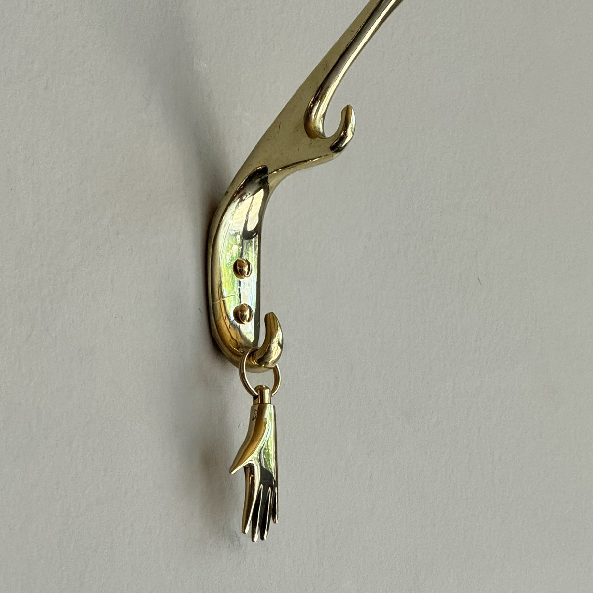 Brass Carl Aubock keyring shaped like a hand on a gray background. 