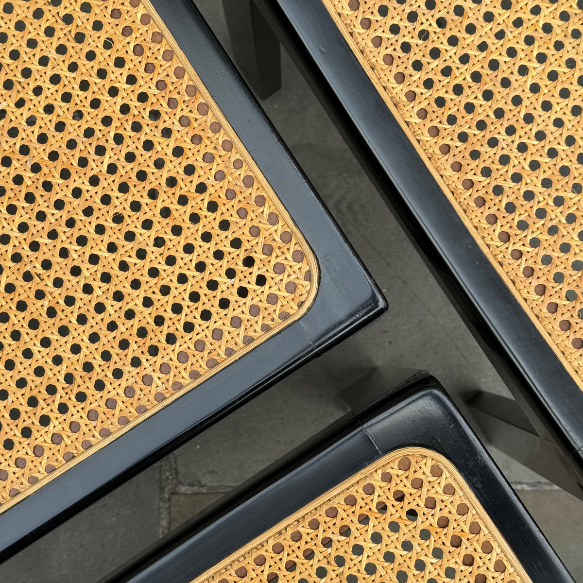 Angular detail of a set of Bankstuhl chairs designed by Willy Guhl, featuring a sleek combination of black lacquered frames and cane seating. These chairs exemplify Guhl's innovative approach to design, blending elegant, modern aesthetics with functional comfort.