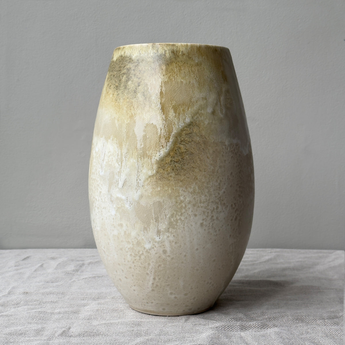 Handmade stoneware art piece vase by Kasper Würtz, in yellow and white, crafted in Denmark shown against a grey wall. 
