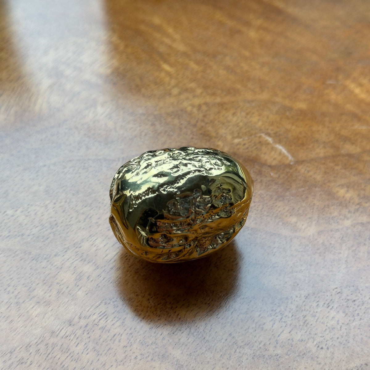 A walnut-shaped paperweight made of cast brass, created in Austria. This piece features modernist design with a blend of organic form and sleek craftsmanship.
