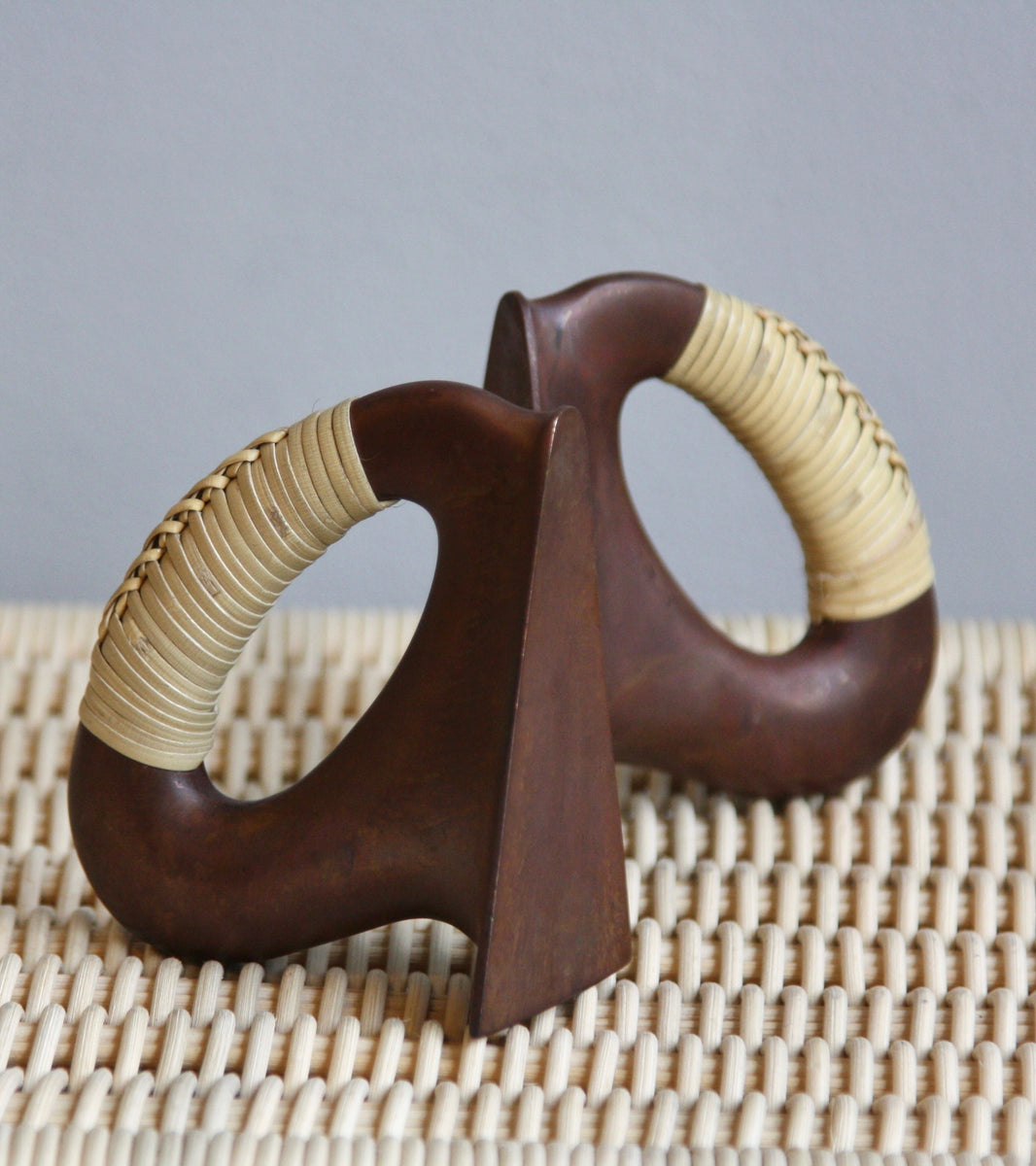 A pair of patinated flat iron bookends by Carl Auböck, crafted in the Werkstätte Auböck workshop, Vienna, Austria. Featuring blonde cane accents, these mid-century modernist pieces exemplify exceptional Austrian design and craftsmanship.